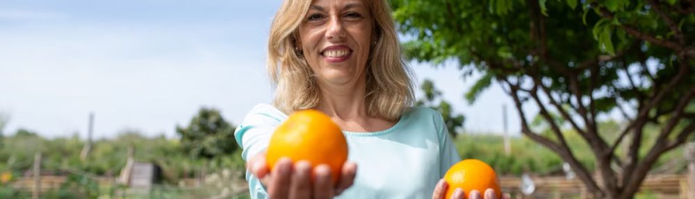 Cheerful woman in garden holding fresh organic oranges, enjoying nature.