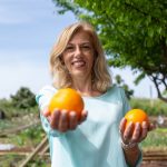 Cheerful woman in garden holding fresh organic oranges, enjoying nature.