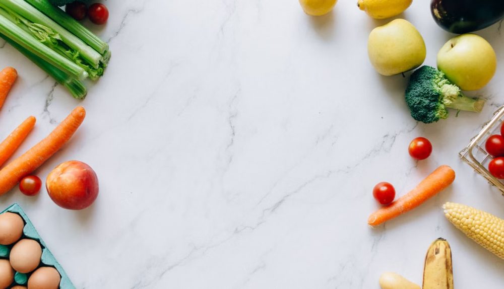 An assortment of fresh fruits and vegetables on a marble background, perfect for healthy lifestyle concepts.